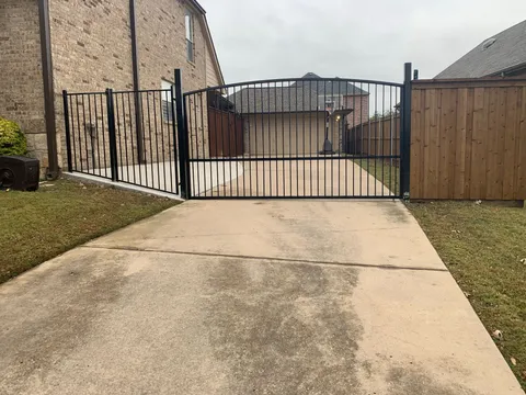 An arched black wrought iron automatic gate across a concrete driveway.